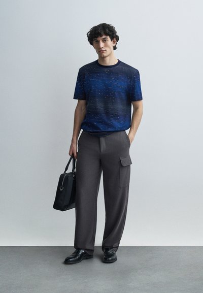 Navy blue, textured short-sleeve t-shirt with light pattern, paired with gray wide-leg cargo pants and black leather shoes. Carrying a black bag.