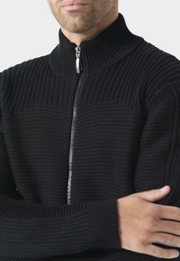 Černý pletený svetr na zip s vysokým žebrovým límcem, zdobený texturovanými vzory a hladkým zipem.