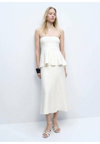 Witte strapless peplum jurk gemaakt van gladde stof, met een vloeiende rok. Gecombineerd met witte sandalen met bandjes en een zwarte armband om de pols.