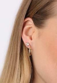 Gouden ringoorbel met een textuur en een kristallen studoorbel. Close-up van het oor, waarbij de sieraden tegen een zachte huid worden belicht.