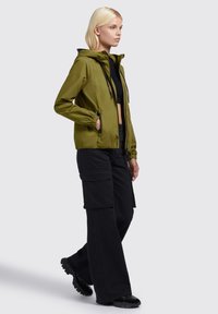 Olive green zip-up jacket with a hood, elastic cuffs, and two side pockets, paired with black cargo pants and black shoes.