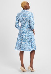 Blau gemustertes Kleid mit kragenförmigem Ausschnitt, langen Ärmeln und einem ausgestellt geschnittenen Rock. Hergestellt aus leichtem Stoff mit einem malerischen Druck.