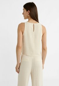 Beige ærmeløs top lavet af linned med en nøglehul detalje på ryggen, parret med matchende beige bukser med frontlommer og en glat tekstur.