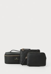 Tres bolsas de cosméticos negras de diferentes formas y tamaños, con materiales lisos y texturizados, cremalleras doradas y un acento floral.