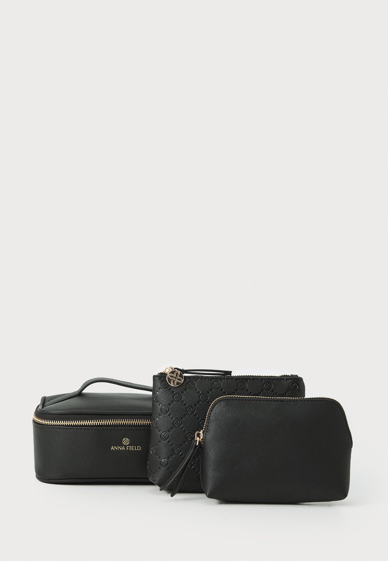 Tres bolsas de cosméticos negras de diferentes formas y tamaños, con materiales lisos y texturizados, cremalleras doradas y un acento floral.
