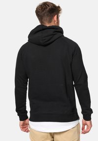 Zwarte hoodie met een trekkoordkap, ribgebreide boorden en zoom. Beschikt over een gladde textuur en een ontspannen pasvorm, weergegeven vanaf de achterkant.