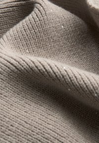 Beige gebreide stof met een gestructureerd ribpatroon en verspreide zilveren pailletten, wat een subtiele glanseffect creëert tegen het zachte materiaal.