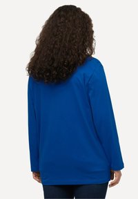 Chemise à manches longues bleue en tissu lisse, présentant une coupe décontractée, un ourlet arrondi et sans motifs ni accents visibles.