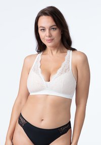 Čipkasti bralette v off-white barvi s valovitimi robovi in globokim V-izrezom; v kombinaciji s črnimi hlačkami s čipkastimi detajli na straneh.