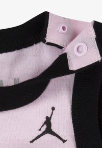 Must ja roosa rõivas ümara kaelusega, millel on palli käes hüppe sooritava mängija graafiline logo ja trukid sulgemiseks.