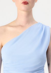 Lichtblauwe één-schouder jurk van zacht materiaal, met plooien aan de zijkant en een gladde textuur.
