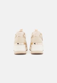 Beige sport schoenen met een gestructureerde afwerking, voorzien van een glanzend gouden accent op de hak, een gevoerde zool en een lusvormige trekband.