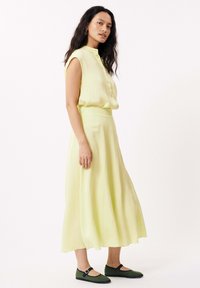 Blouse sans manches jaune clair avec des boutons, associée à une jupe fluide de la même couleur, portée avec des ballerines vertes.