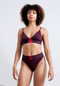 Set de bralette și thong burgund din Calvin Klein. Material moale, design minimalist, cu un band în contrast roșu cu logo la talie și bust.