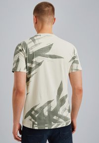 T-shirt à manches courtes de couleur crème avec un motif de feuilles abstraites vertes. Fabriqué en coton doux, avec un col rond et une coupe décontractée.