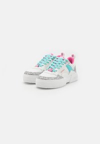 Baskets blanches avec une pointe argentée pailletée, des lacets turquoise, des accents roses, et une semelle épaisse pour plus de hauteur et de soutien.