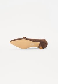 Brune suedestiletthæl med spids tå, lille ankelrem og en tekstureret gummisål. Et subtilt logo er prægget på sålen.