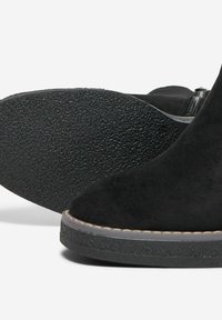 Black suede ankle boots with textured rubber soles, rounded toes, and visible stitching detail along the sole edge. Zipper closure on side.