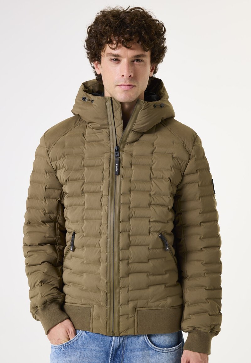 Chaqueta corta acolchada en verde oliva, con cierre frontal con cremallera, capucha, puños acanalados y bolsillos laterales con cremalleras negras. Tejido texturizado.