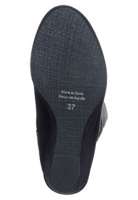 Suela de zapato de ante negro con patrón de goma texturizado, marcada "Hecho en España" y tamaño "37". El diseño es aerodinámico con una silueta suave.