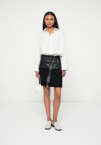 Λευκό πουκάμισο με ρίγες και μακριά μανίκια, μαύρη δερμάτινη φούστα με υφή και φερμουάρ, λευκή τσάντα με πτυχές και ανοιχτό γκρι εσπαντρίγιες.