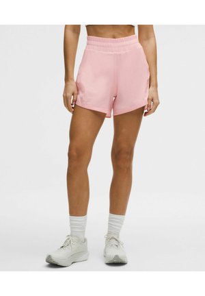 Kvinde iført lyserøde atletikshorts med elastisk linning, hvide sokker og hvide løbesko mod en ensfarvet baggrund.