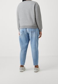 Harmaa rento collegepaita, jossa on ribbatut hihansuut, yhdistettynä vaaleansinisiin korkeavyötäröisiin farkkuihin. Kenkinä hopeansävyiset urheilukengät.