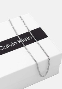 Sølv kædetræk på en hvid Calvin Klein æske. Kæden har et glat, rundt led-design med en subtil glans og minimalistisk stil.