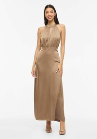 Robe longue en satin de couleur beige chaud, avec un col licou, un corsage froncé, un détail œillet et une silhouette lisse et fluide.