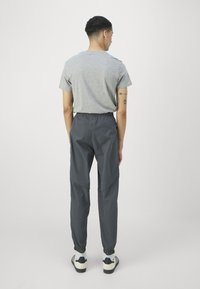 T-shirt gris à manches courtes, associé à un pantalon gris foncé avec une taille élastique et des chevilles resserrées. Baskets représentées ci-dessous.