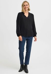 Blusa nera a maniche lunghe con scollatura a V e polsini arricciati, abbinata a pantaloni blu navy a taglio slim e stivaletti neri alla caviglia. Tessuto dal tocco morbido.
