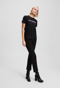 T-shirt nera a maniche corte con logo "KARL LAGERFELD", abbinata a pantaloni neri slim-fit e stivaletti con tacco. Texture liscia in tutto il capo.