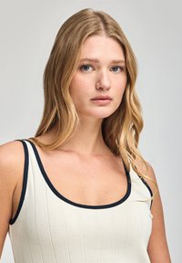 Cream-colored ribbed top with navy trim, featuring a scoop neckline and adjustable straps, made from a soft, textured fabric.