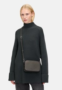 Maglione grigio scuro a maglia con colletto alto, abbinato a una piccola borsa a tracolla rettangolare in pelle. Tessuto strutturato e tracolla regolabile.
