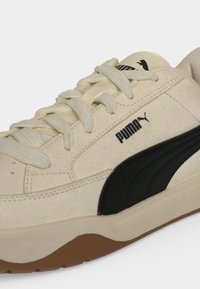 Λευκό-κρεμ παπούτσι Puma με σουέντ υφή, μαύρη λωρίδα στο πλάι, λογότυπο, μπεζ κορδόνια και καφέ λαστιχένια σόλα.
