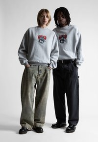 Felpe grigie con grafiche colorate, jeans larghi beige e neri e scarpe nere. Linee pulite e stile casual.