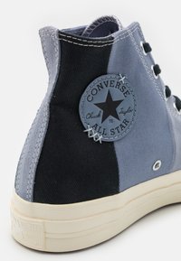 Baskets montantes en toile, composées de sections bleues et noires. Présentent un patch circulaire avec le logo Converse et une semelle en caoutchouc blanc.