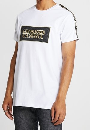 Weißes kurzärmeliges T-Shirt mit einem schwarzen und goldenen rechteckigen Aufnäher mit der Aufschrift „GLORIOUS GANGSTA“ vorne, getragen von einer Person mit dunkler Jeans.