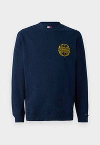 Sudadera de cuello redondo azul marino con el logo amarillo "Tommy Jeans New York City" en el lado izquierdo del pecho y una pequeña bandera en el puño izquierdo.