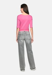 Fitted pink long-sleeve top paired with high-waisted, light gray wide-leg jeans. Notable features include a belt and decorative stitching.
