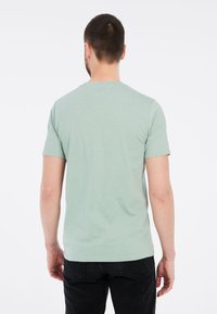 Jasnozielona koszulka z krótkim rękawem, okrągłym dekoltem, uszyta z miękkiego, lekkiego materiału. Posiada prosty, czysty design.