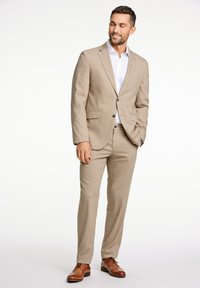 Beige pak met een gestructureerde afwerking, colbert met één knoop, bijpassende broek en bruine leren schoenen, gecombineerd met een witte overhemden.