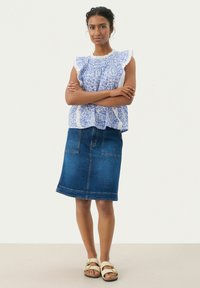 Top corto a maniche corte blu con fiori e ruches, abbinato a una gonna a tubino in denim scuro. Il modello indossa sandali beige con cinturini.