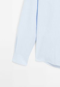 Camicia azzurra a maniche lunghe realizzata in tessuto morbido, dotata di polsini con bottone e un orlo leggermente curvato. Texture liscia, senza motivi.