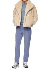 Fluffy beiger Mantel mit breitem Kragen, hellblauem Pullover, lockeren lavendelfarbenen Hosen und silbernen Sneakers mit schwarzen Akzenten.