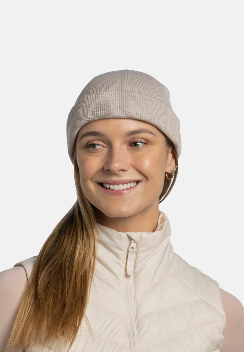 Light beige knitted beanie with a ribbed texture, worn with a cream sleeveless puffer vest. The beanie is snug-fitting and simple in design.