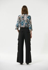 Langmouw blouse met een patroon van blauwe bloemen en een zwarte high-waisted broek met zijvakjes en een wijde broekspijpen.