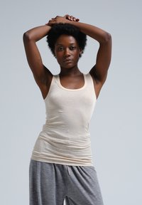 Beige katoenen tanktop met een ronde hals, gecombineerd met grijze sweatpants met trekkoord, gedragen door een persoon met een afro haarstijl.