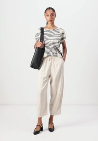 Haut court rayé gris et blanc, pantalon crème avec cordon de serrage, et sac bandoulière noir. Le mannequin porte des chaussures à talons noires. Fond uni.