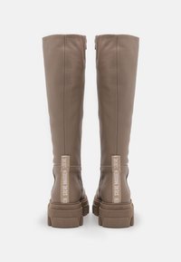 Bottes montantes en cuir beige texturé avec une semelle en caoutchouc épaisse et des accents de panneaux latéraux avec logo en blanc. Fermeture éclair à l'arrière.